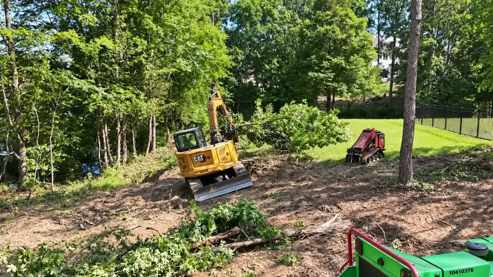 Excavator clearing woods next to a chipper