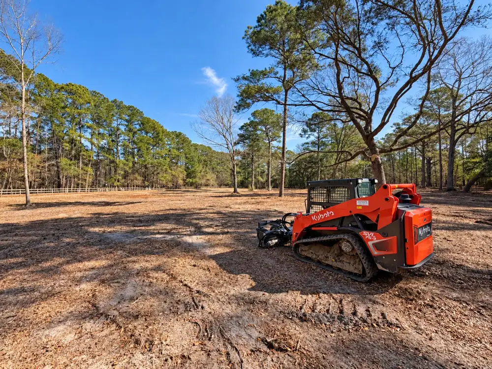Red Kubota track loader with a mulcher on a freshly cleared lot in the pines